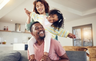 Dad playing with daughter on shoulders with mom behind them