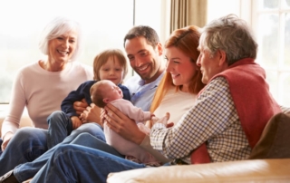Family sitting on couch while dad passes baby off to grandpa