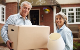 Two older individuals looking at camera while moving into new home